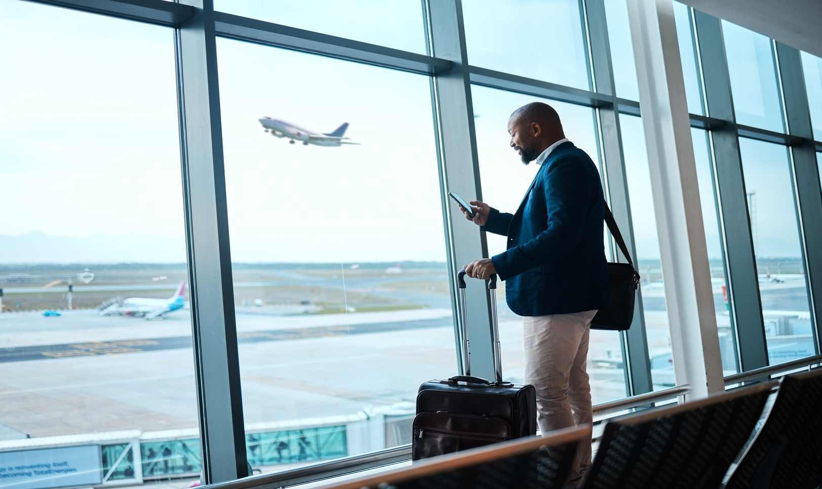 Black man with phone, airport window and plane taking off, checking flight schedule terminal for business trip.