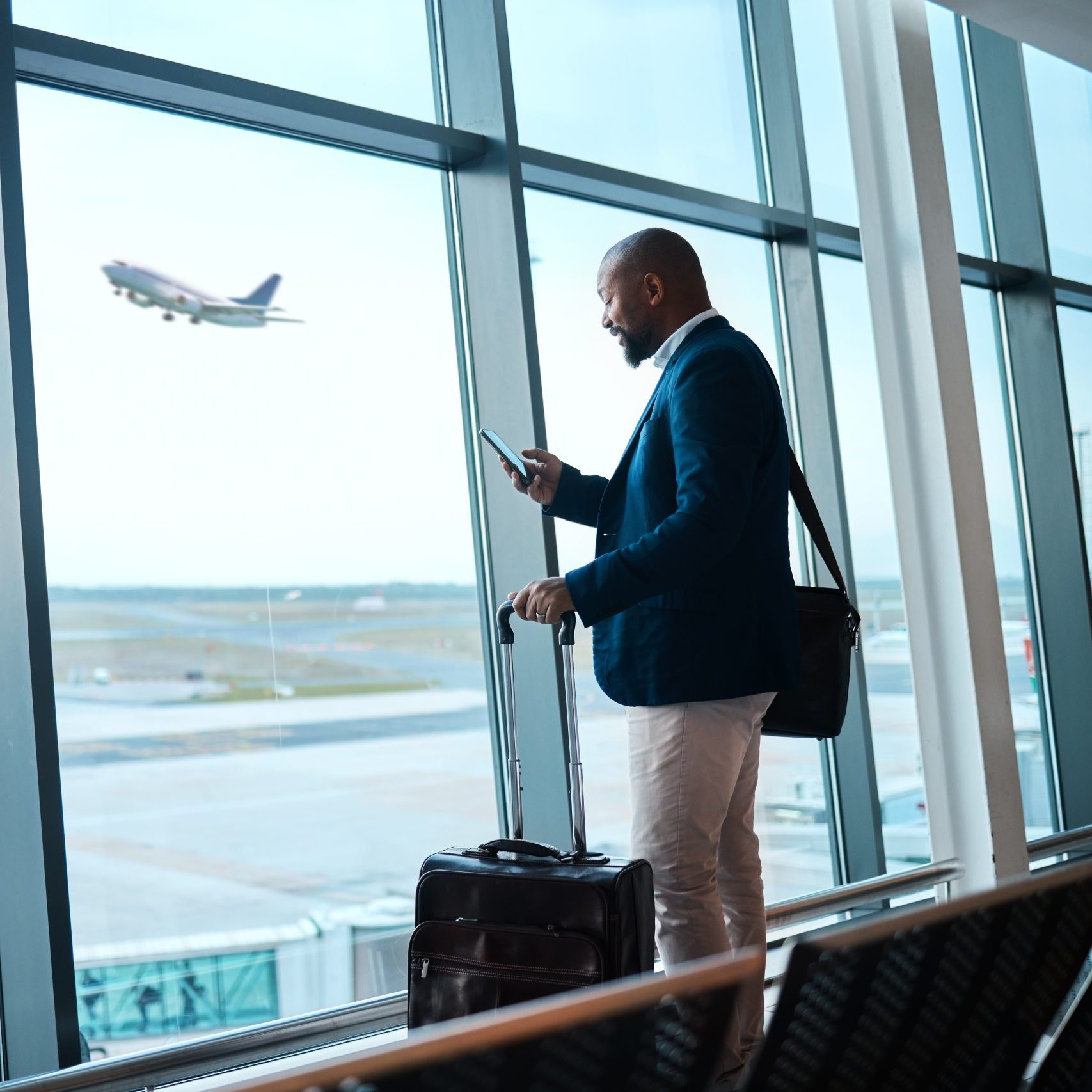 Black man with phone, airport window and plane taking off, checking flight schedule terminal for business trip.
DST Business Travel Stock Photo